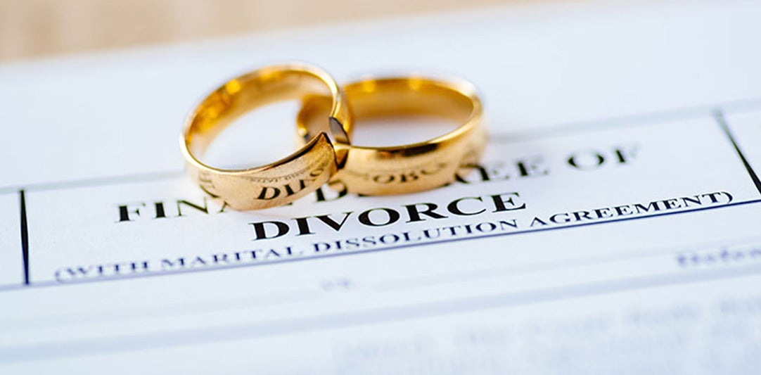 Two gold wedding bands rest on a legal document with 'DIVORCE' clearly printed.