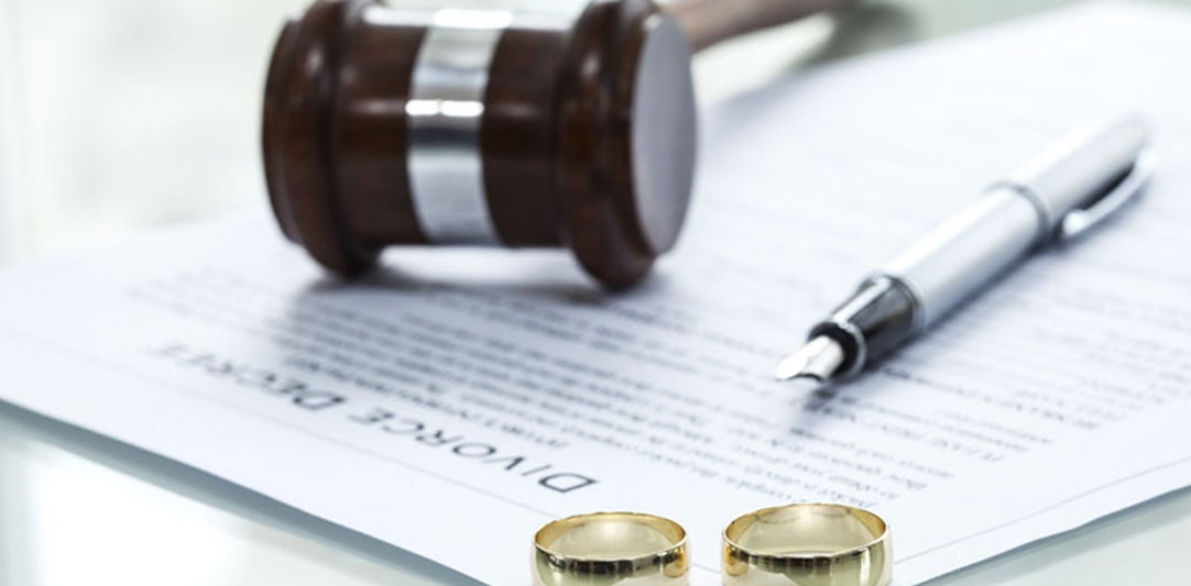 A gavel, fountain pen, and two wedding rings rest on a document titled 'DIVORCE DECREE.'