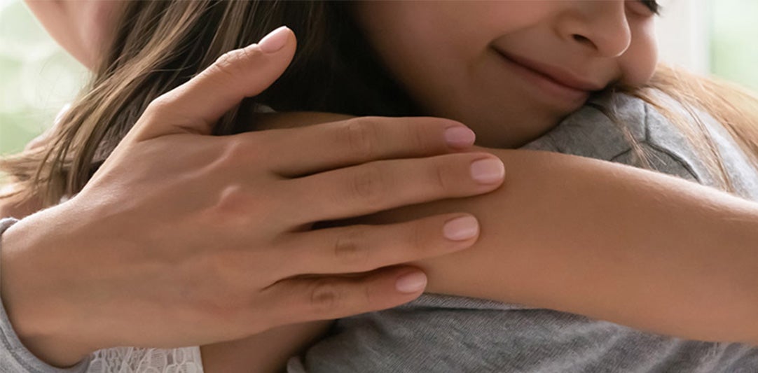 A close-up of an adult's hand hugging a child, who smiles sweetly while leaning into the embrace.